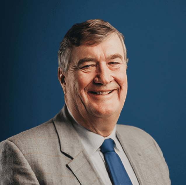 Studio portrait of Arnaud Dalais in a light checked jacket and blue tie against a deep navy background