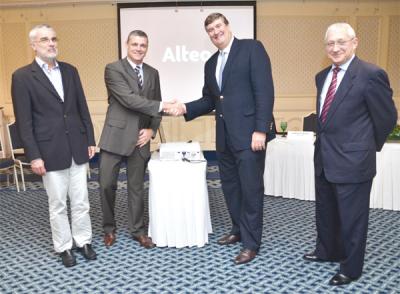 Executives at a Mauritian corporate announcement event, shaking hands in front of a presentation screen