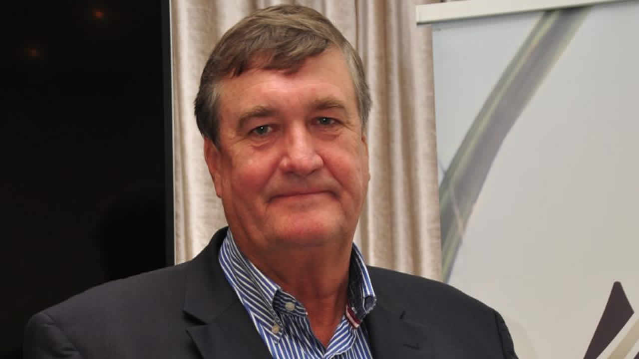 Arnaud Dalais in a dark jacket and striped shirt at a conference, a presentation screen behind him